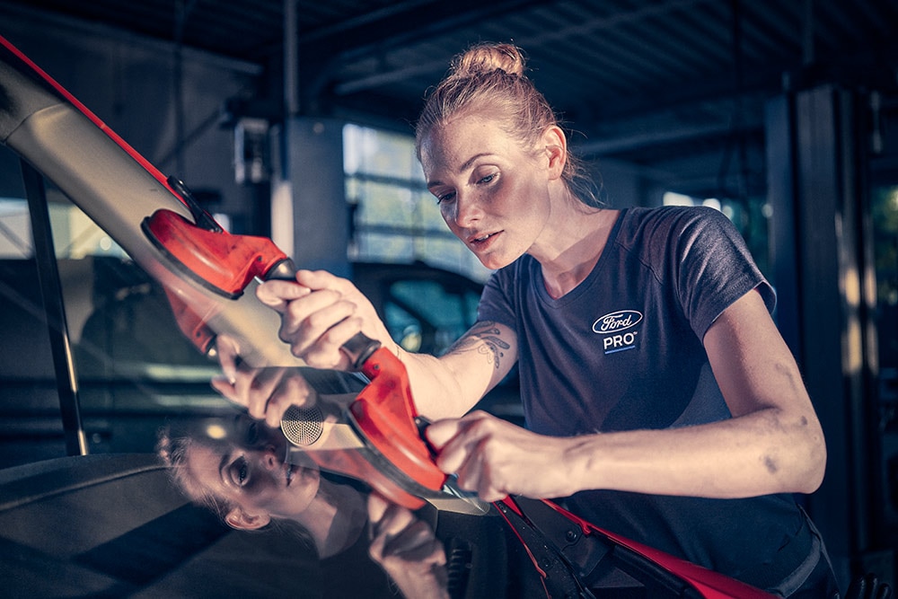 A technikus egy autó szélvédőjén dolgozik egy garázsban.