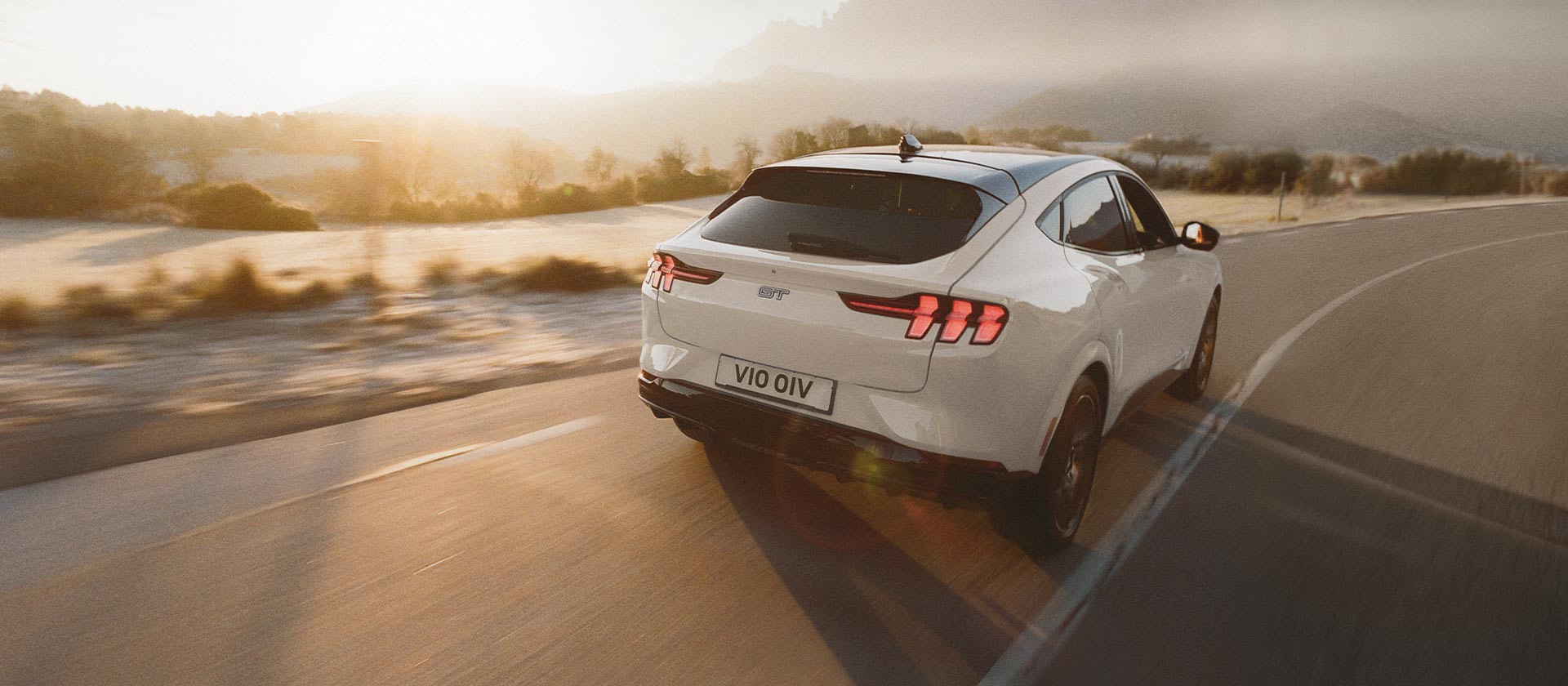 Ezüstszínű Ford Mustang Mach-E elektromos jármű hosszú nyílt úton halad.