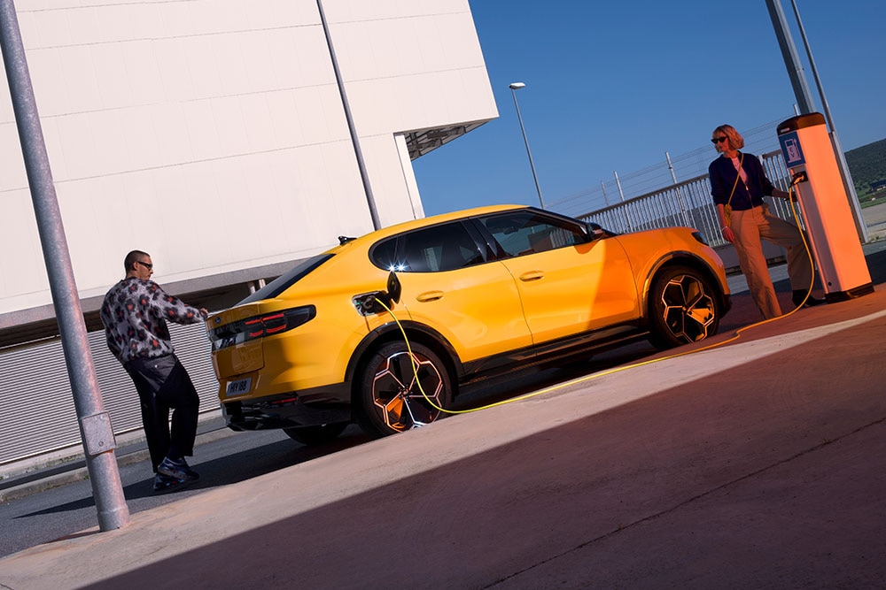 Sárga Ford Capri EV-t tötő emberek egy köztéri töltőállomáson.