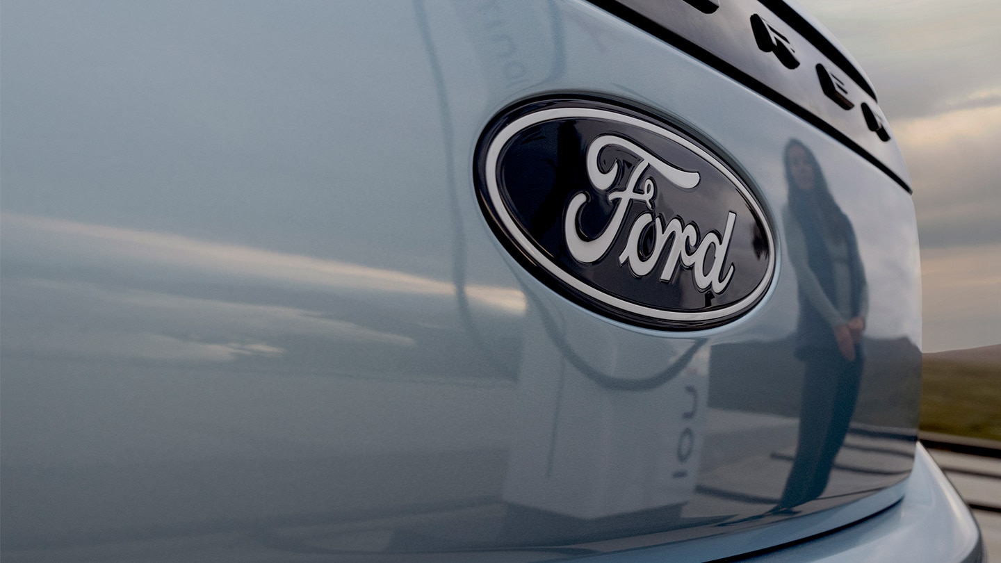 Ford logó egy kék elektromos Ford Exploreren, az autóban tükröződő köztéri töltőállomással.