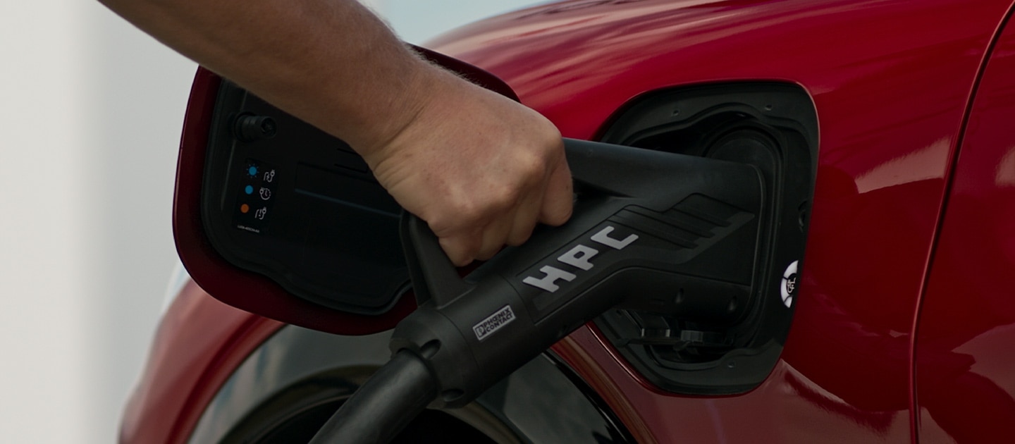 Közelkép egy piros Ford EV-ről, melyet egy köztéri HPC (High Power Charger) töltőállomáshoz csatlakoztatnak, a gyors köztéri EV-töltéshez.