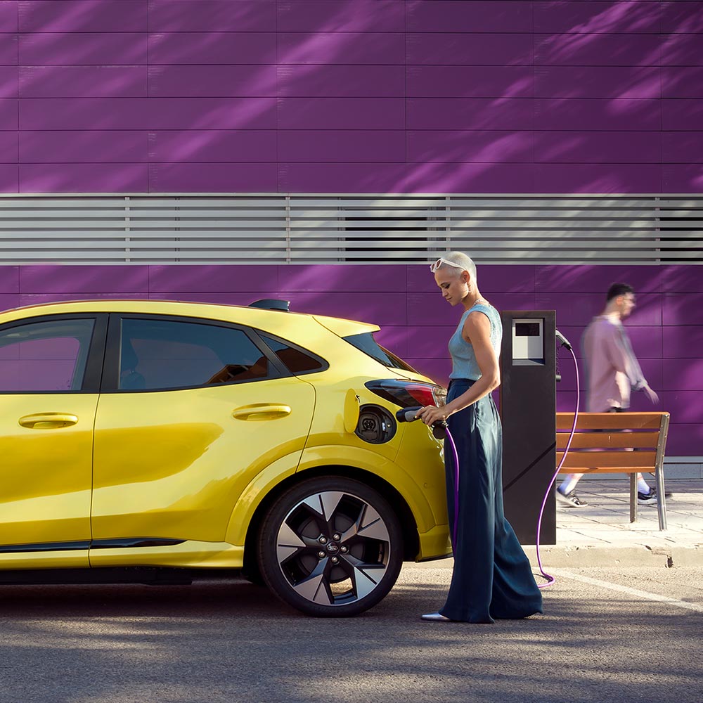 Egyszerű elektromos töltéshez sárga Ford Puma Gen-E-t köztéri töltőállomáshoz csatlakoztató személy.