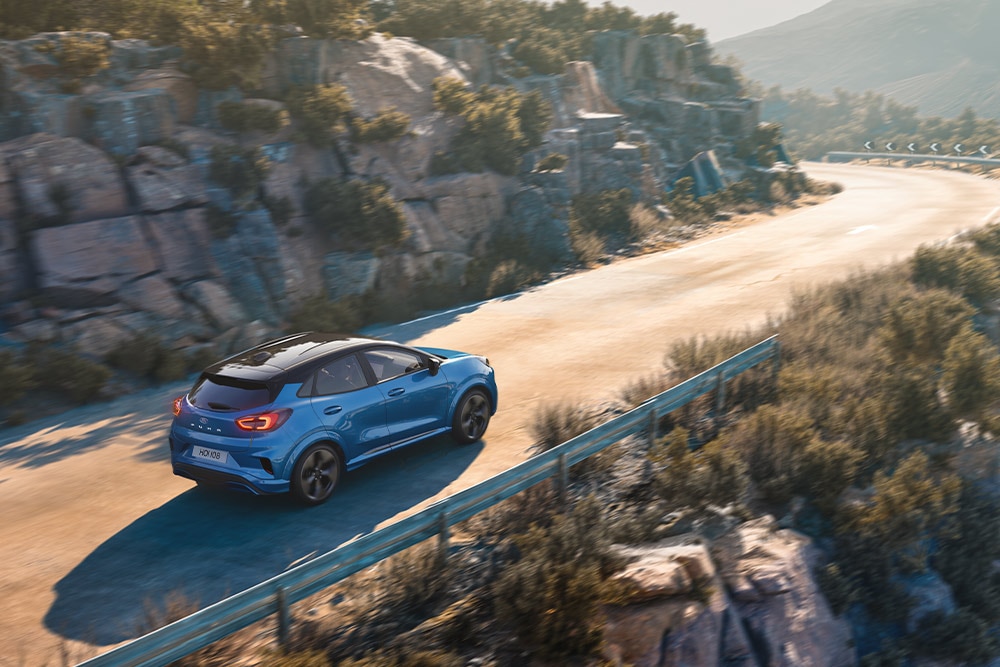 Egy kanyargós hegyi úton halad egy kék Puma Gen-E.