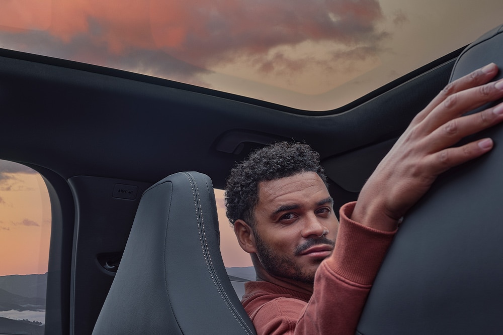 Egy férfi ül egy autóban naplementekor, kezét az egyik ülés háttámlájára támasztva.