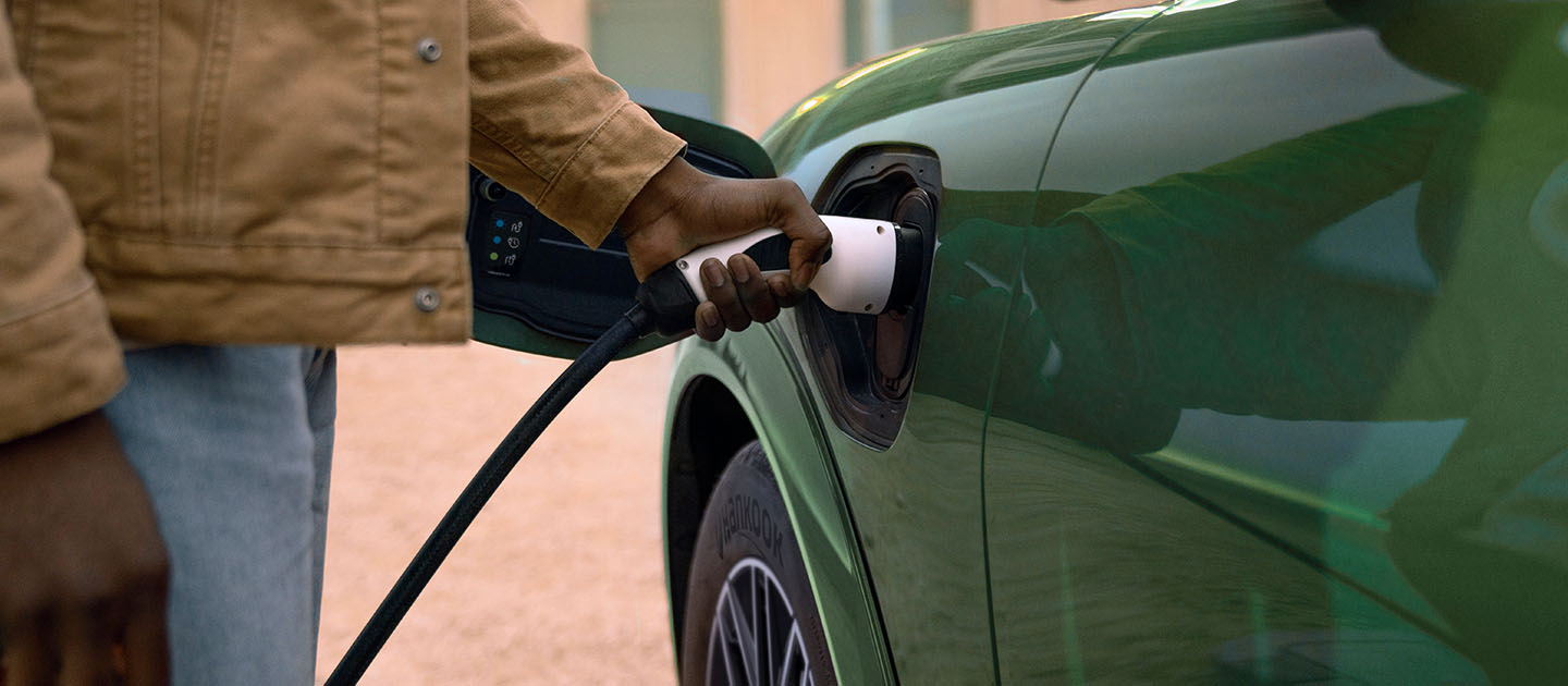 Valaki elektromos töltőkábelt csatlakoztat a zöld elektromos Ford Mustang Mach-E-hoz.