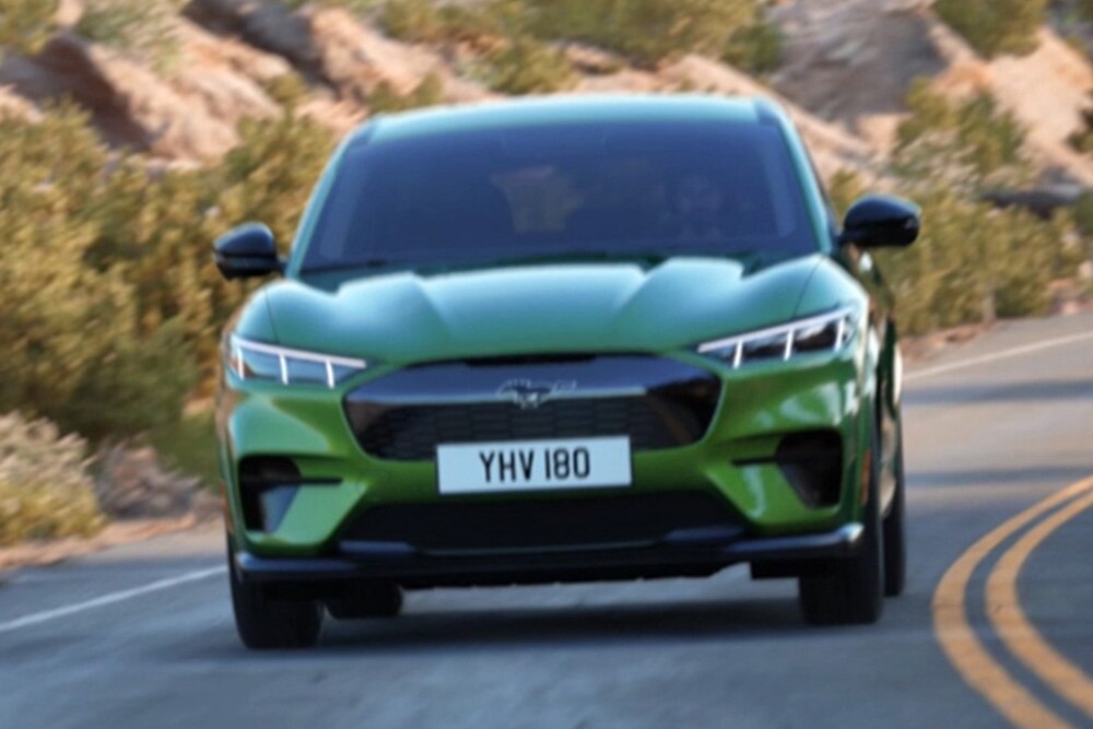Hegyi úton haladó zöld Ford Mustang Mach-E elölnézetből. 