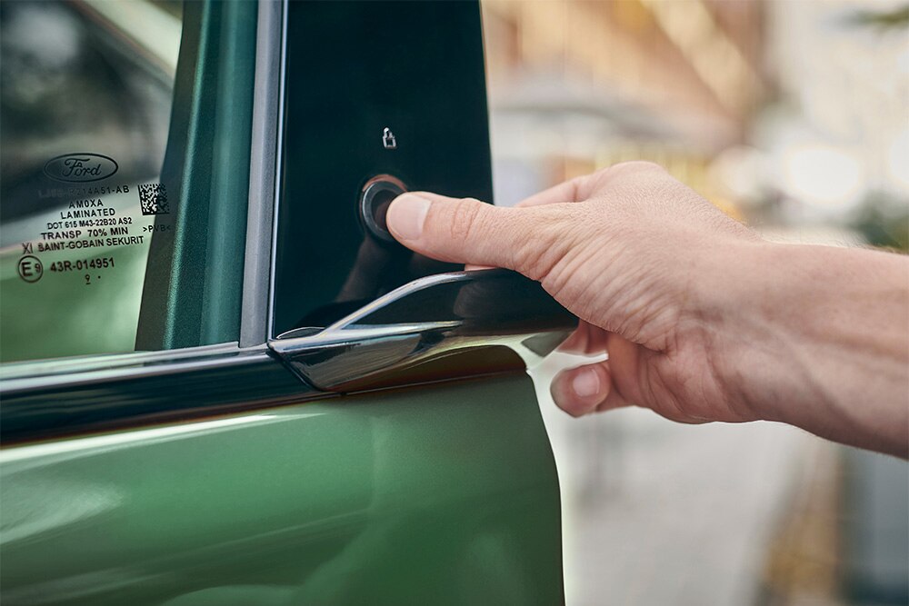 Közelképen az E-zár rendszert aktiváló kéz egy zöld Ford Mustang Mach-E ajtógombjával. 