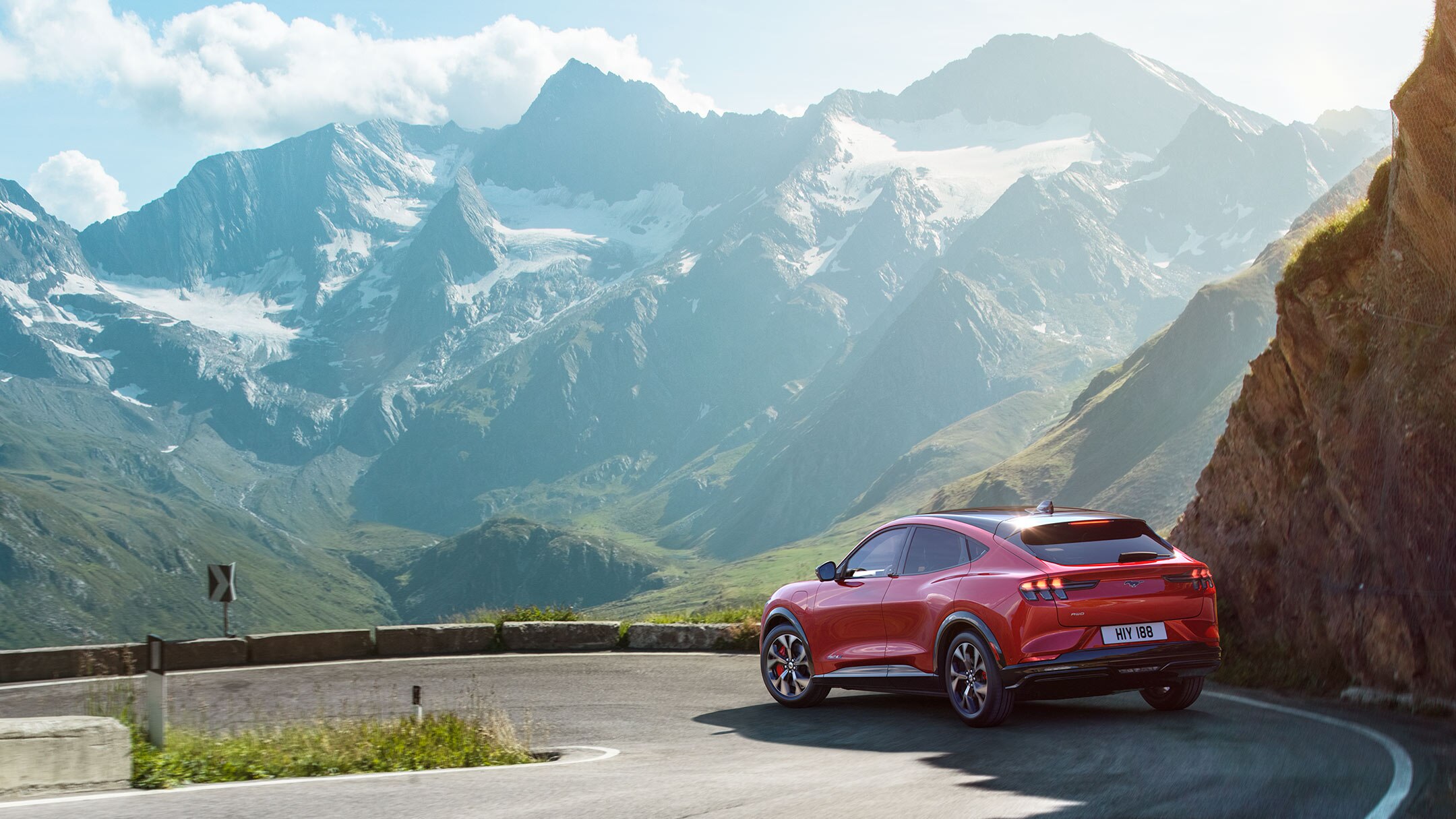 A red All-New Ford Mustang Mach-E driving on the road in the mountains