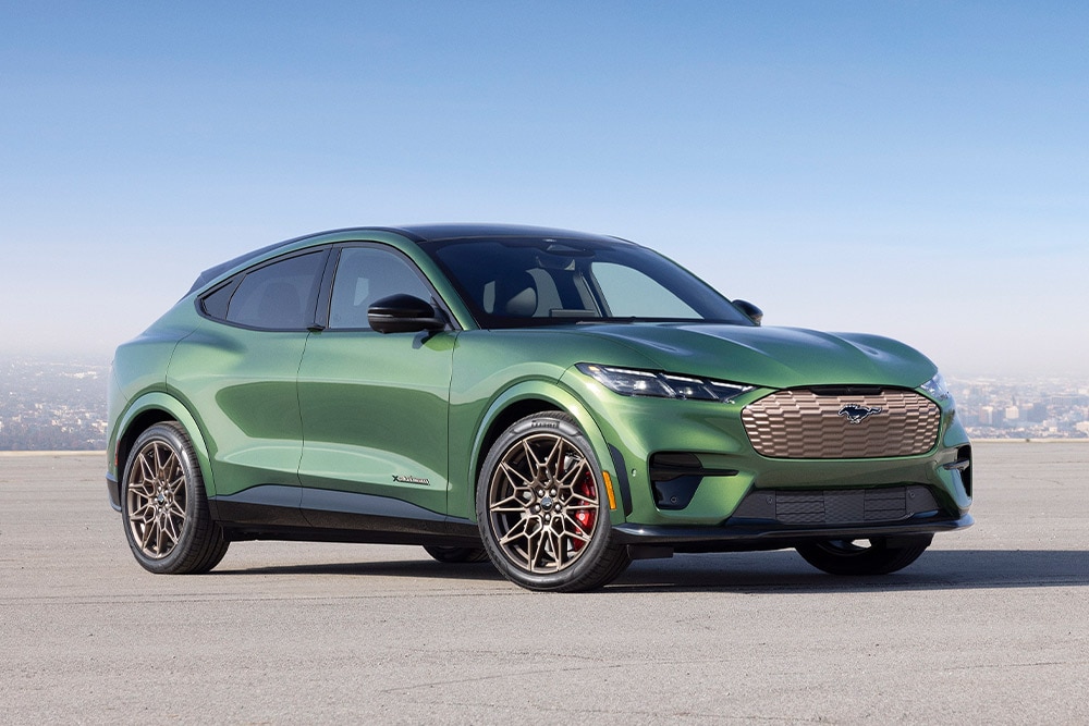 Zöld Ford Mustang Mach-E parkol egy város körvonalai előtt.