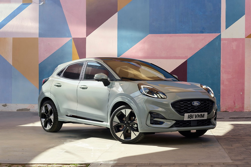 Ezüstszínű Ford Puma SUV parkol egy színes geometrikus falfestmény előtt.