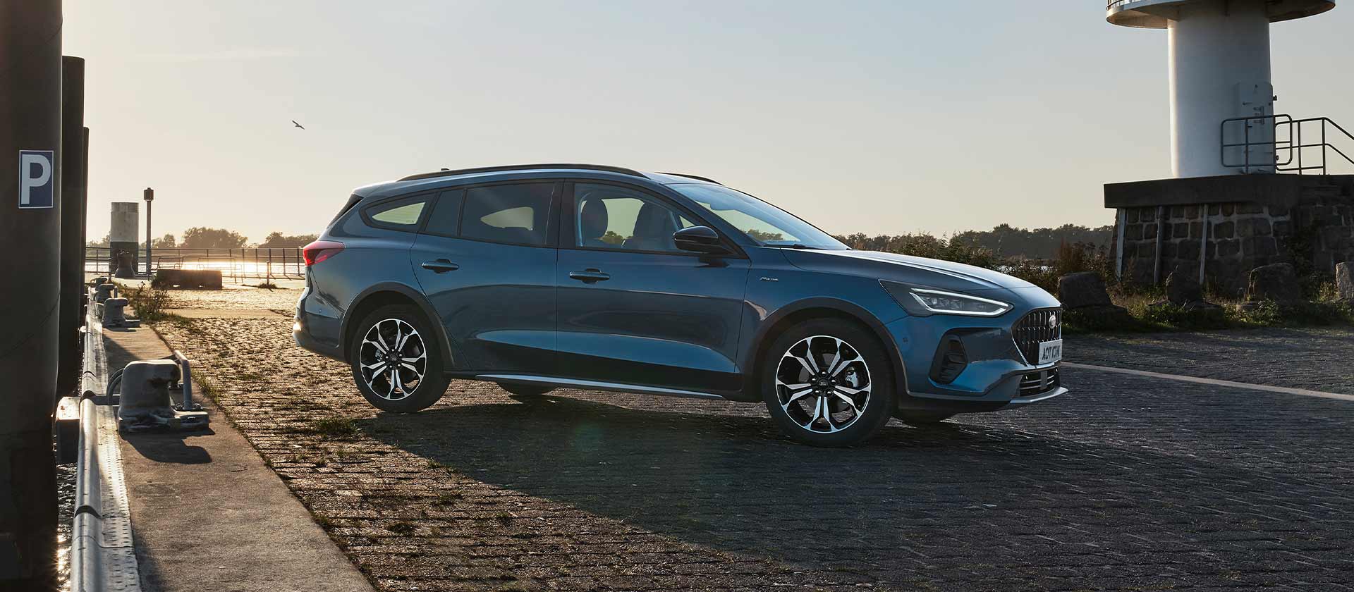 Kék Ford Focus Active kombi parkol egy macskaköves úton, egy fehér világítótorony közelében.
