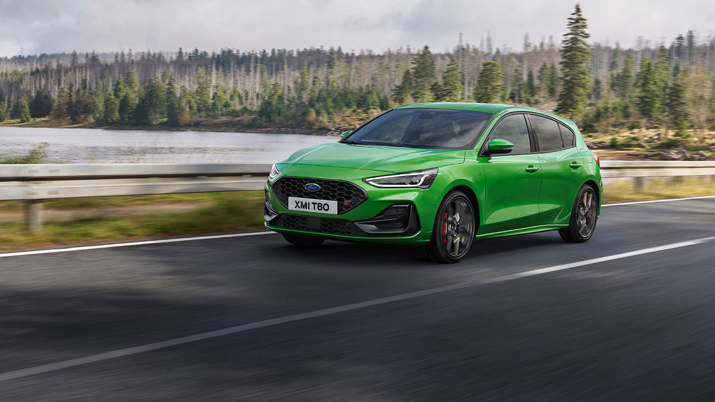 Egy Ford Focus ST Mean Green színben halad egy fákkal szegélyezett úton.