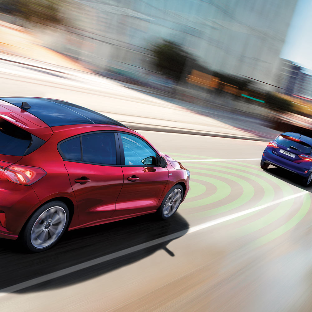 Grafika egy piros Ford Focus-ról, mely kék vonalakkal jelzett érzékelők segítségével érzékeli az előtte haladó járművet a vészfékezési rendszer részeként.