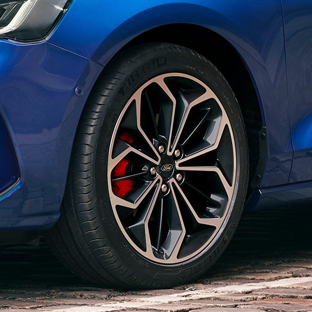 Közelkép a kék Ford Focus szürke keréktárcsájáról és piros féknyergéről.