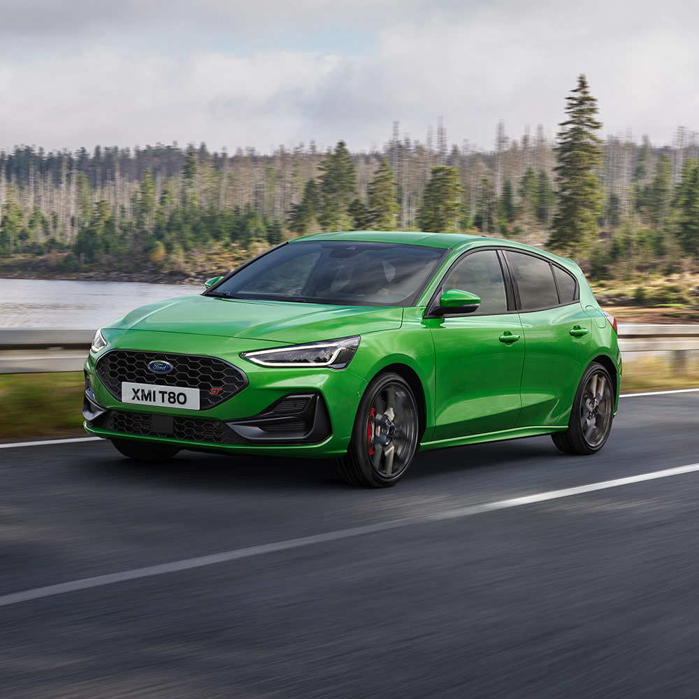Egy Mean Green színű Ford Focus ST kanyargós, fákkal szegélyezett úton halad.