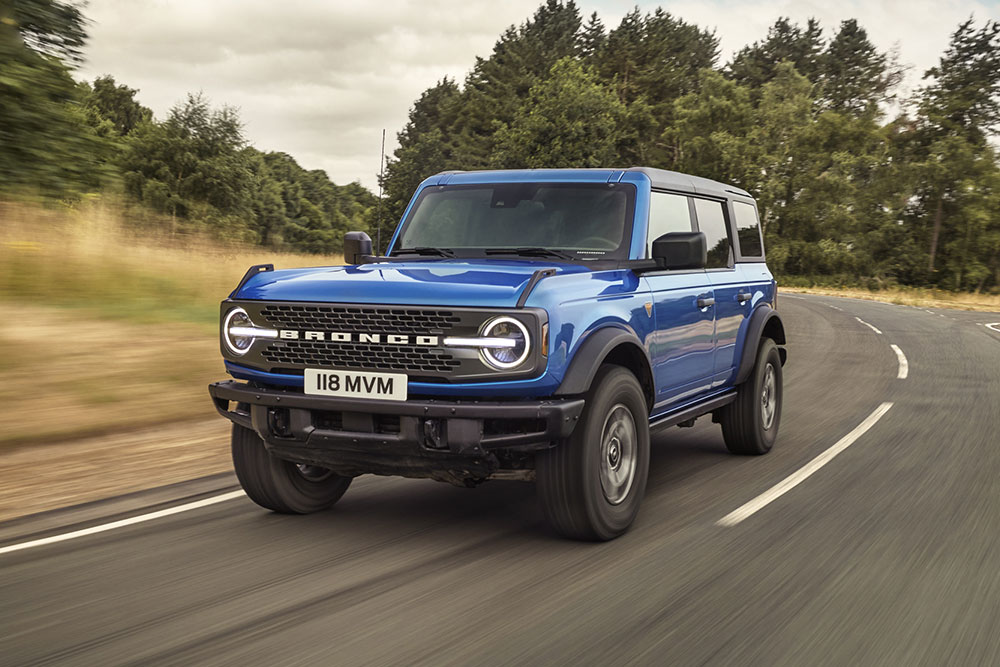 Elölnézet a új Ford Bronco kék színű modelljéről, amely egy vidéki úton halad.