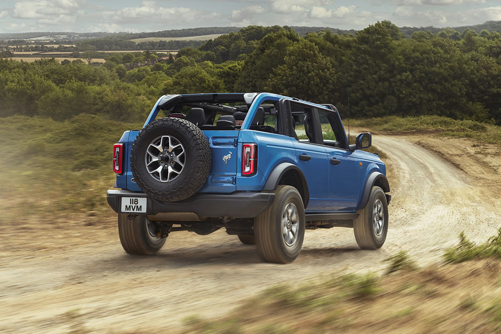 Egy kék Ford Bronco hátsó nézete, amint egy vidéki tájat szel át.