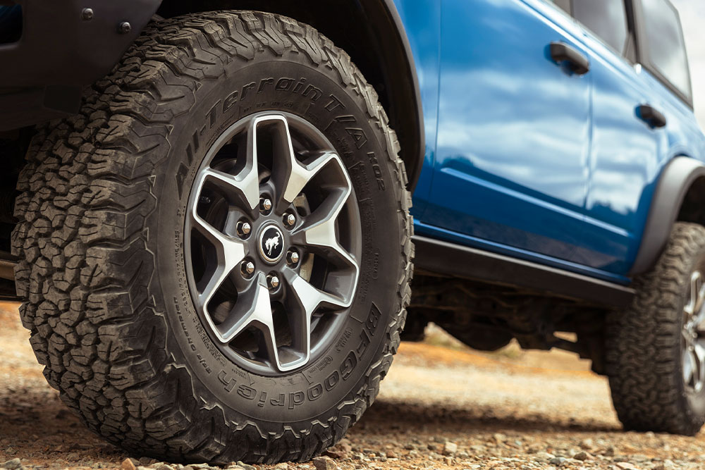 Közelkép egy kék Ford Bronco terepjáró gumiabroncsairól.