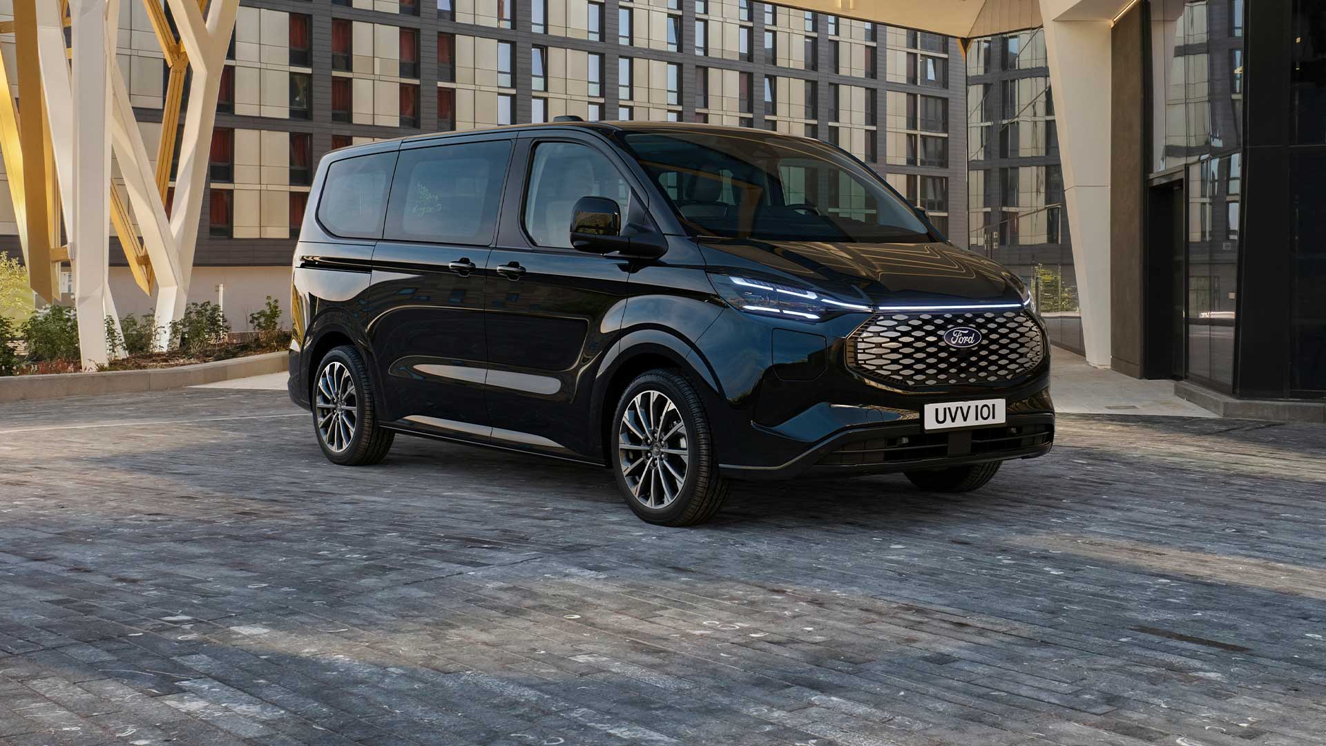 Fekete Ford E-Tourneo Custom egy modern épület előtt parkol.