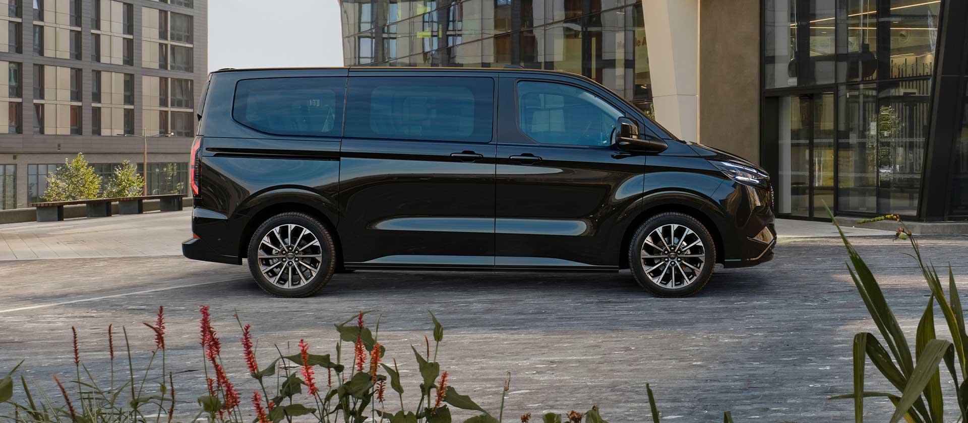 Fekete Ford E-Tourneo Custom egy modern épület előtt parkol.