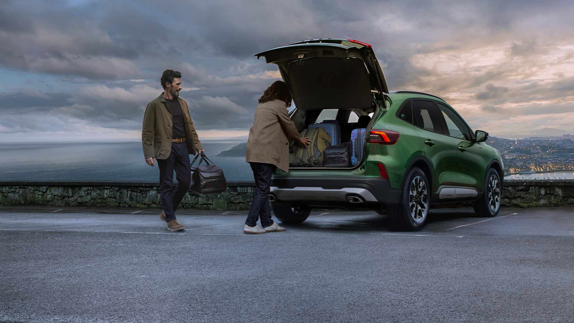 Két ember több bőröndöt pakol a Ford Kuga tágas csomagterébe.