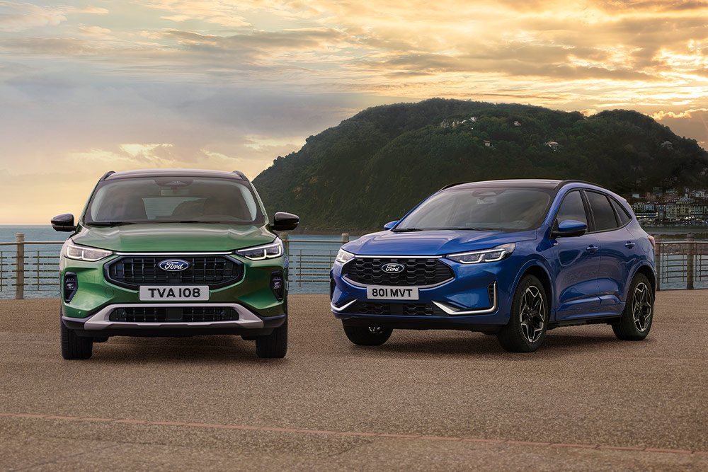 Egy zöld Ford Kuga Active és egy kék Ford Kuga ST Line parkol egymás mellett egy tengerparti parkolóban. 