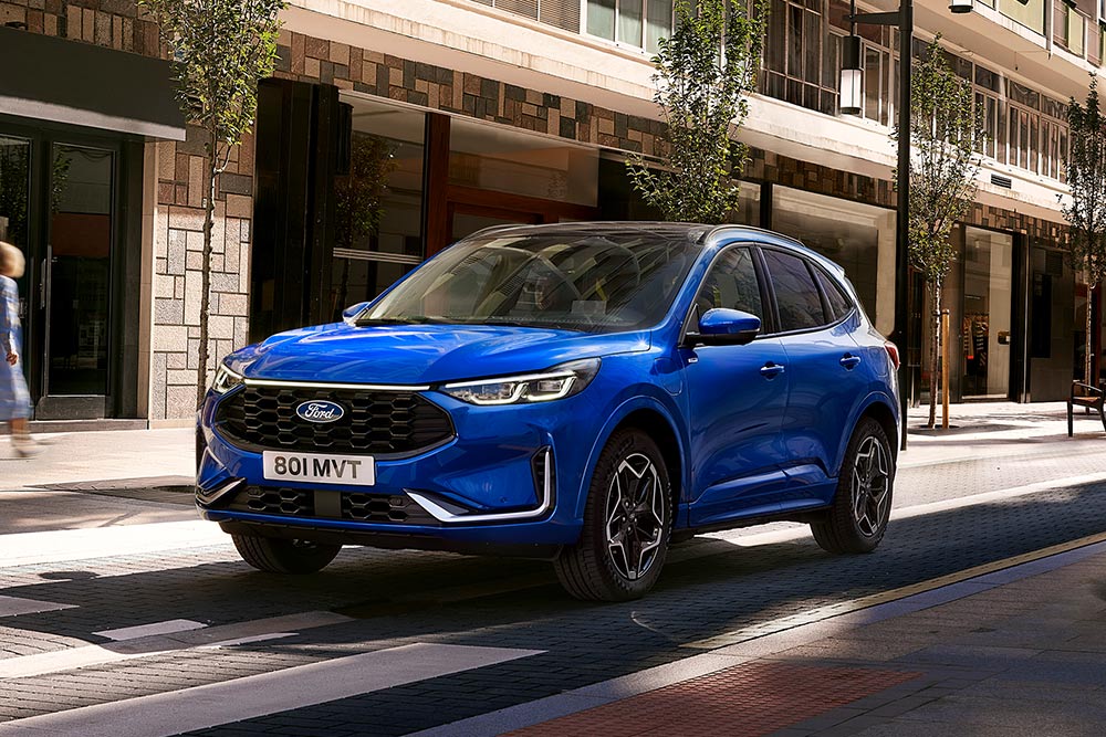 Egy Desert Island Blue karosszériaszínű Ford Kuga ST Line egy lakóövezeti parkolóban áll. 