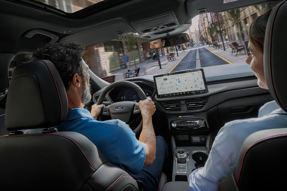 Két ember ül egy  Ford Kuga autóban, mely városi utcán halad a 12,3"-os digitális műszerfal útmutatásait követve.