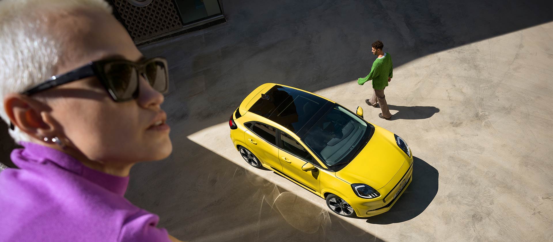 Sárga elektromos Ford Puma Gen-E® modell madártávlatból. Az előtérben egy lila ruhás személy áll.