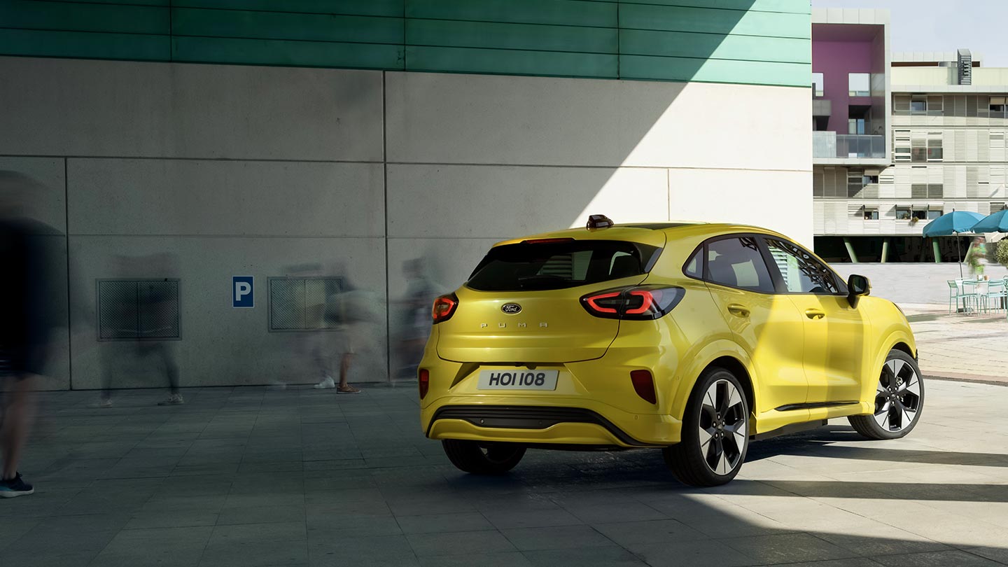 Híd alatt parkoló sárga, elektromos Ford Puma Gen-E® jármű hátulnézetből.