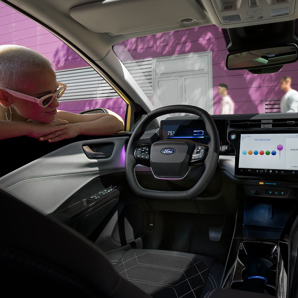 Egy személy az ablakon át nézi az elektromos Ford Puma Gen-E® utasterében lévő nagy infotainment képernyőt.