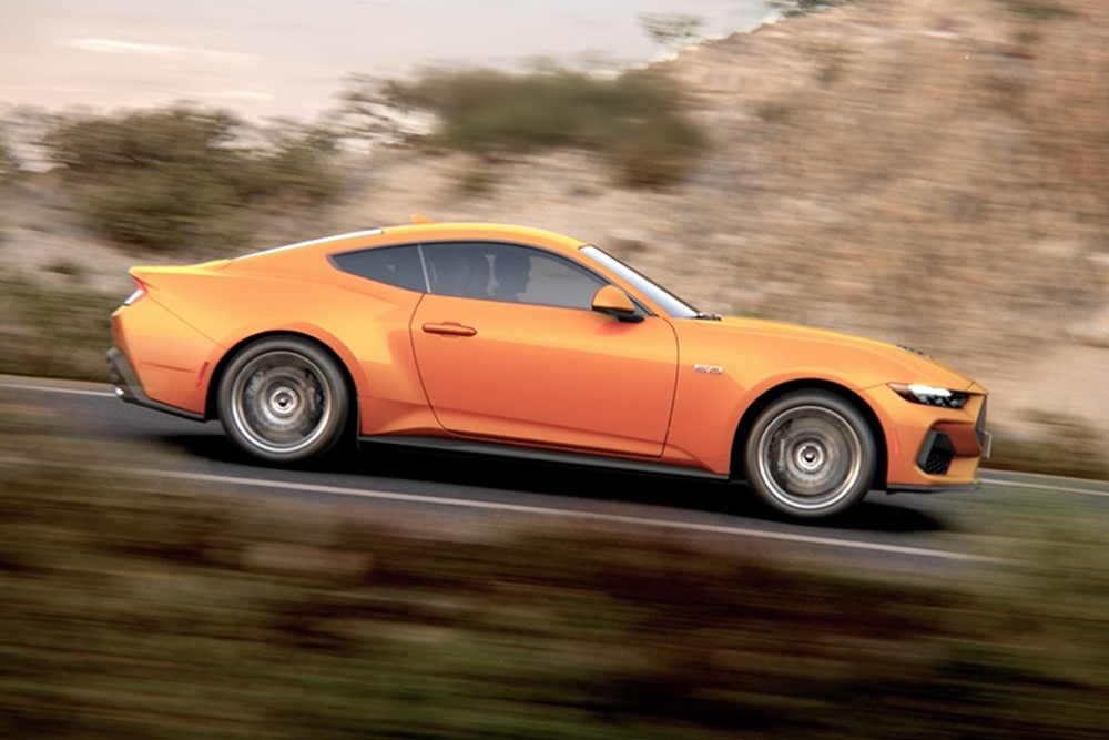 Oldalnézet a Ford Mustang GT Fastbackról Orange Fury színben, úton haladva