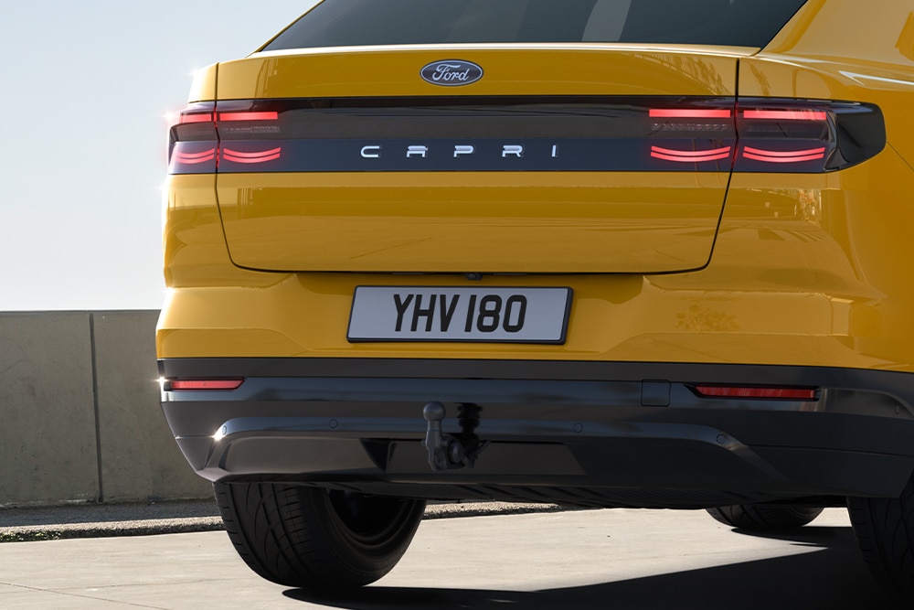 Városi úton haladó sárga Ford Capri® hátulnézetből.