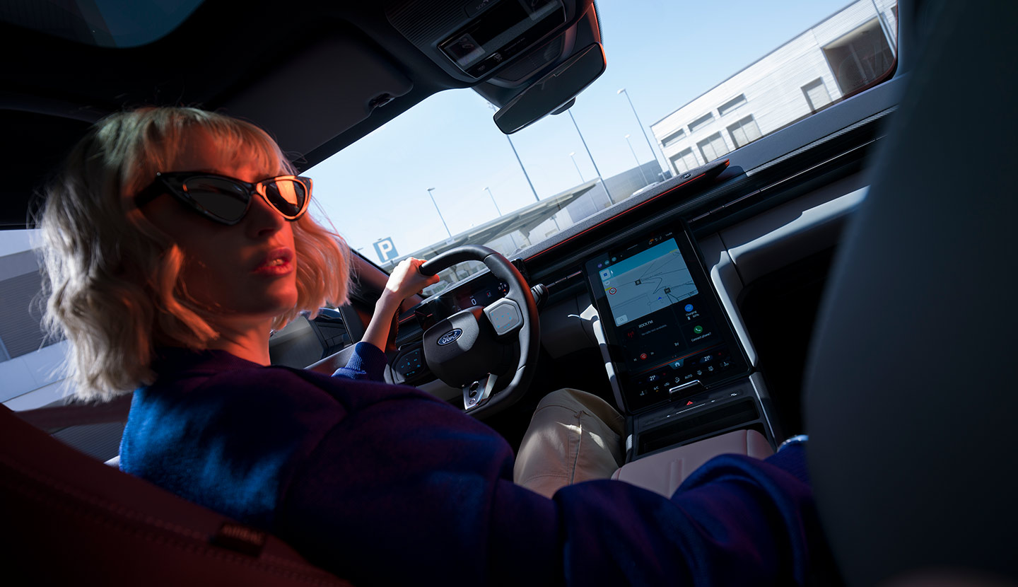 Egy nő ül egy leparkolt Ford Capri® volánjánál, valamint látjuk a kormánykereket és a nagy méretű SYNC® Move érintőképernyőt is.