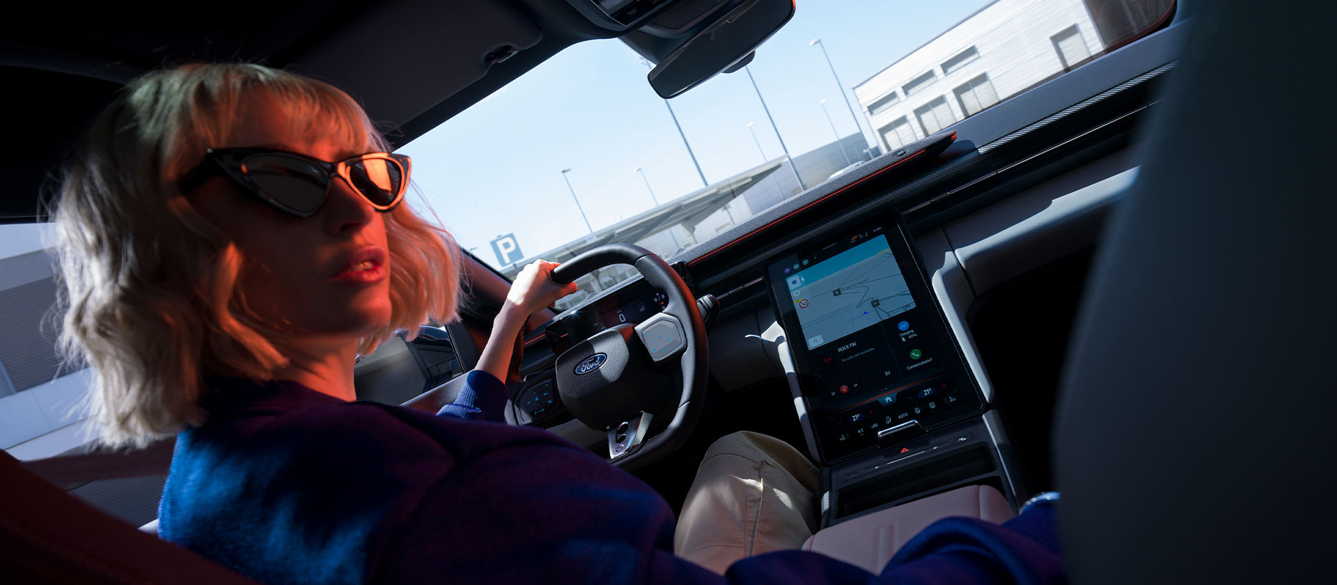 Egy nő ül egy leparkolt Ford Capri® volánjánál, valamint látjuk a kormánykereket és a nagy méretű SYNC® Move érintőképernyőt is.