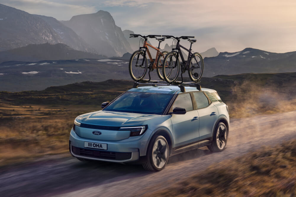 Kék Ford Explorer suhan a földúton, két kerékpárral a tetőtartón. 