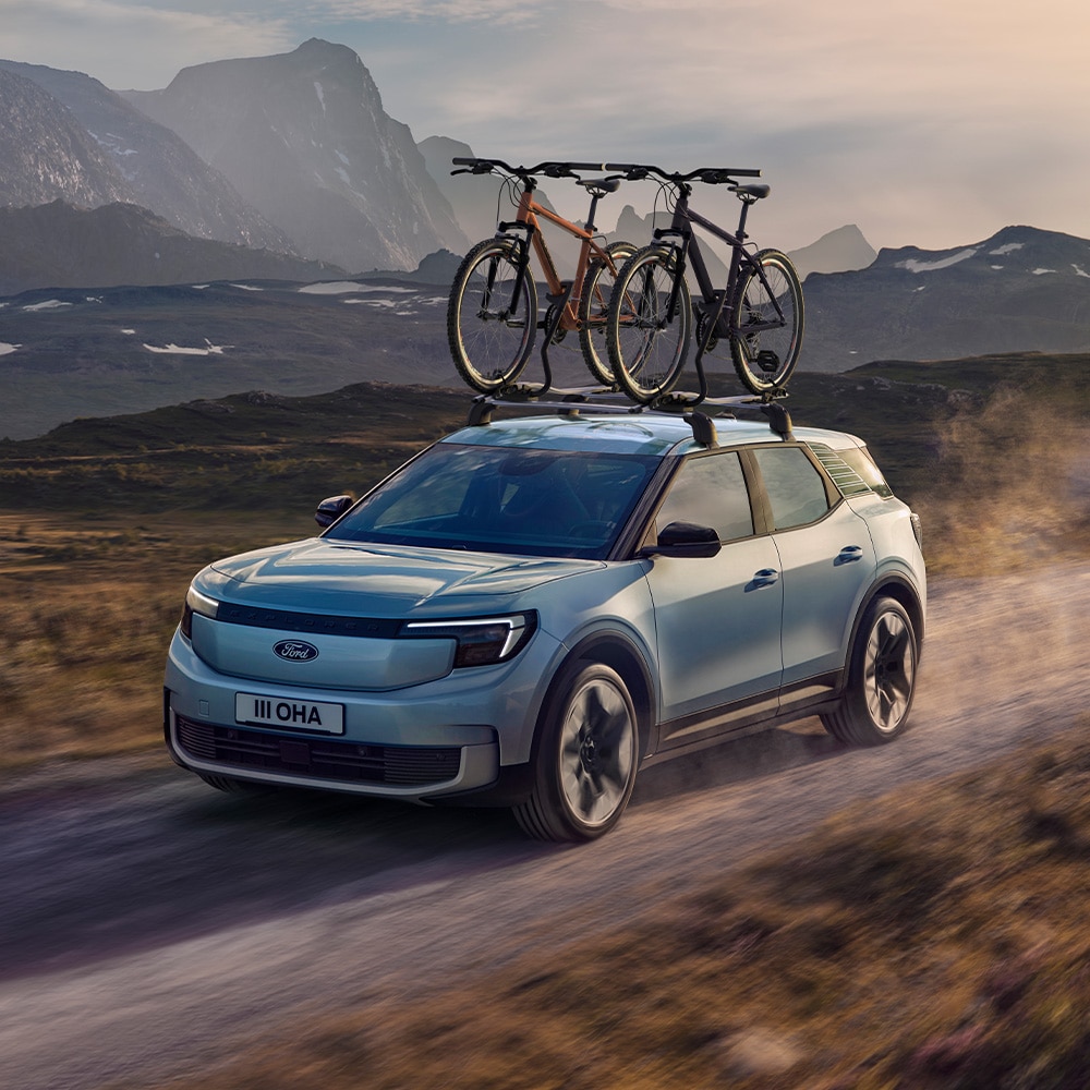 Kék Ford Explorer suhan a földúton, két kerékpárral a tetőtartón. 