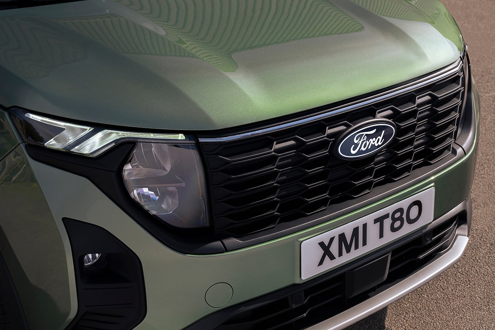 Egy zöld Ford Tourneo Courier egyterű első rácsa és fényszórója.
