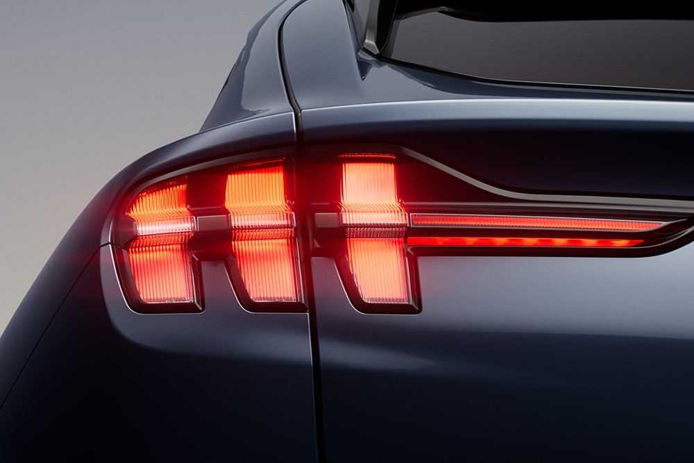 Közelképen látjuk egy Ford Mustang Mach-E sportautó világító hármas hátsó lámpáit.