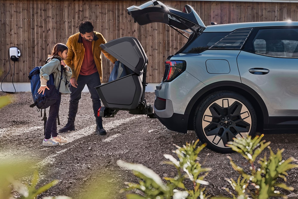 Egy férfi és egy gyermek áll egy Ford Explorer SUV nyitott csomagtartójánál, és egy összecsukott babakocsit pakolnak be.