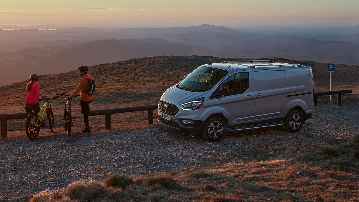 Ford Transit Custom Active oldalnézetből, zárt ajtóval, naplementével és két kerékpárossal 