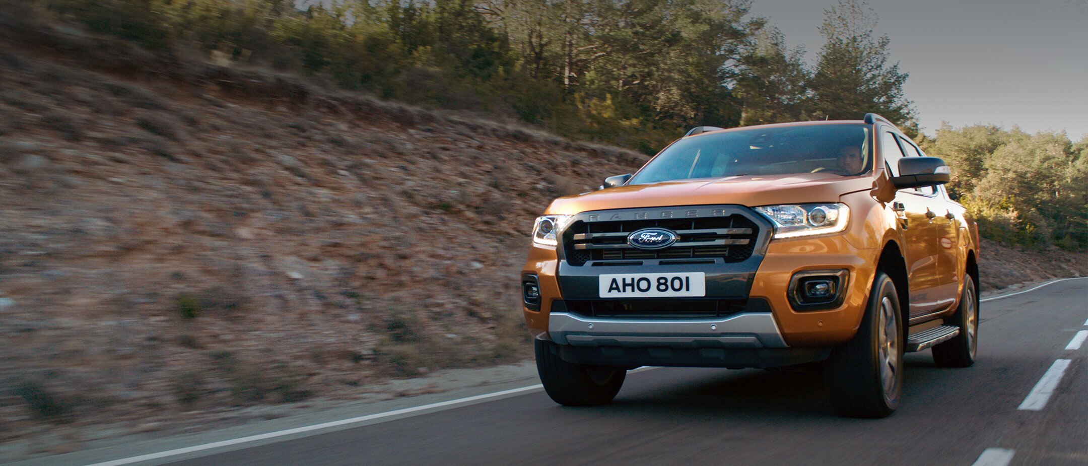Orange Ford Ranger Wildtrak driving through a forest, front three quarter view Orange Ford Ranger Wildtrak driving through a forest, front three quarter view