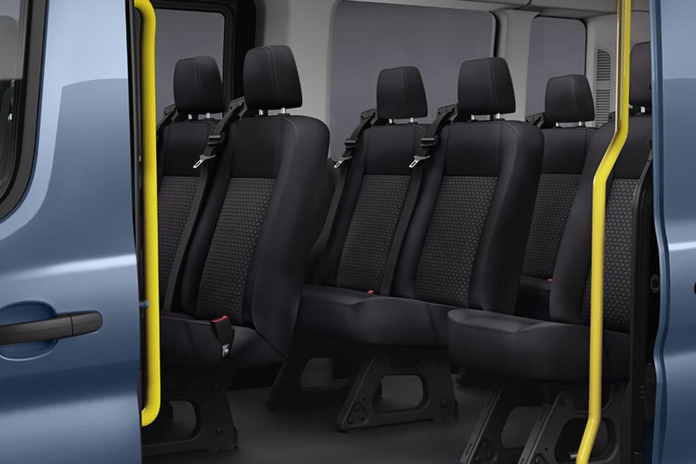 Interior of a Ford Transit Minibus showing black passenger seats and a yellow grab handle near the open door.