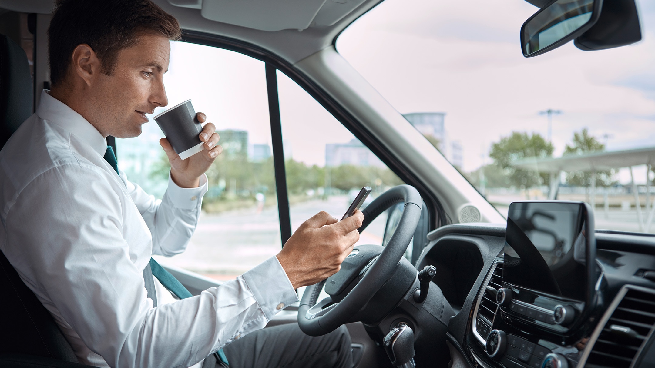 Driver sitting behind driving wheel drinking coffee