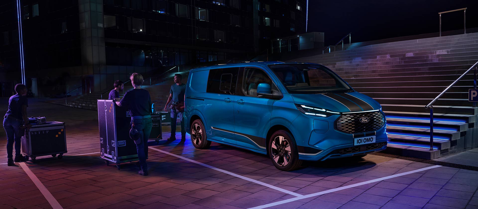 Egy kék Ford E-Transit Custom elektromos áruszállítóba éjszaka pakolnak.