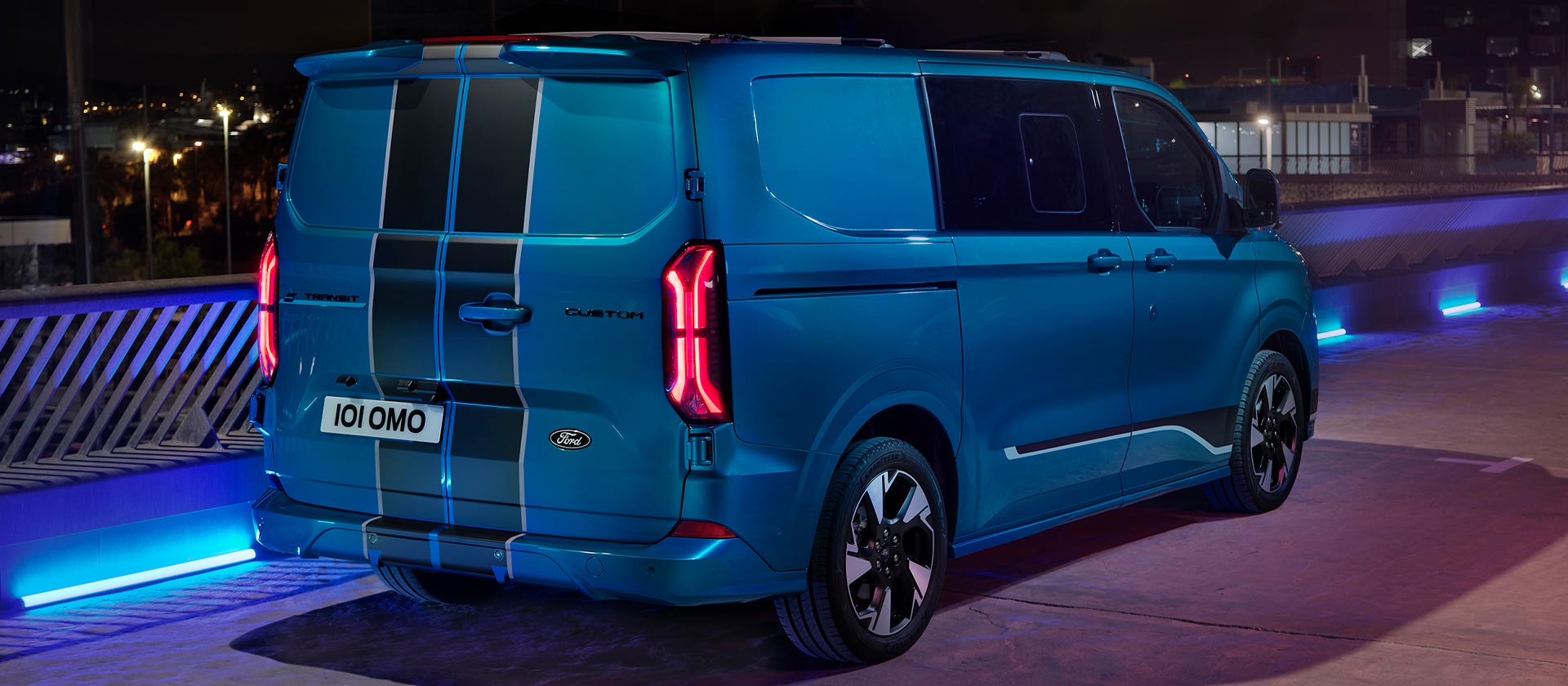 Egy kék Ford E-Transit Custom Sport duplakabinos elektromos személyszállító, hátulnézetből.