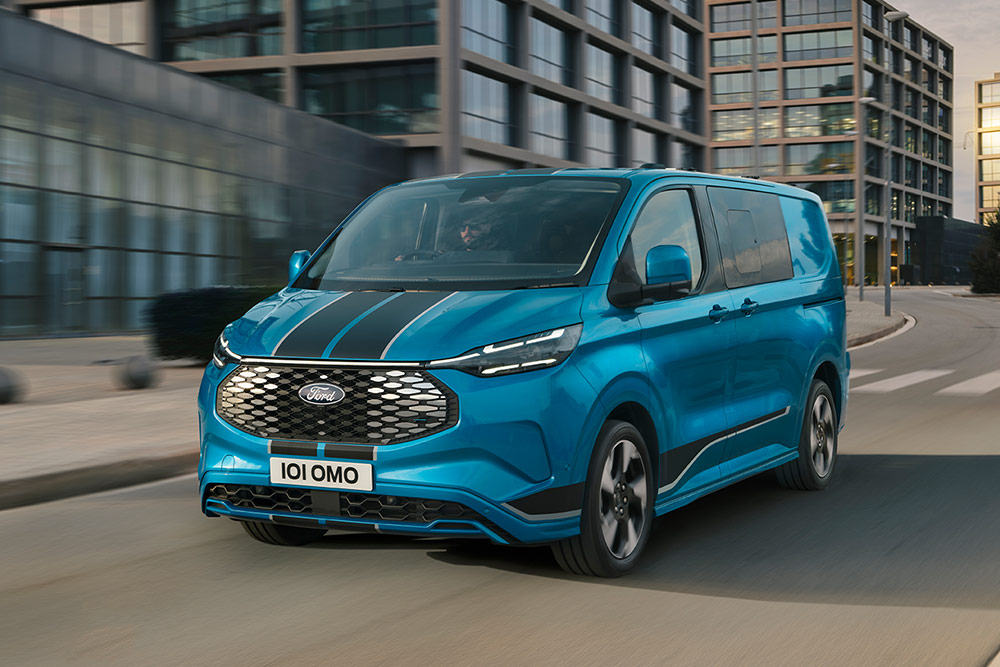 Egy kék Ford E-Transit Custom Sport dupla kabinos áruszállító egy városban halad az úton.