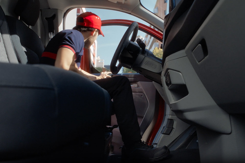 Valaki egy piros Ford E-Transit Custom elektromos áruszállító vezetőülésében ül.