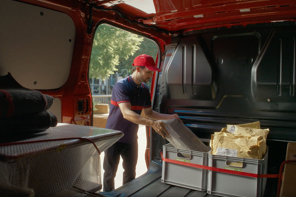 Delivery driver loading packages into a red Ford E-Transit Custom.