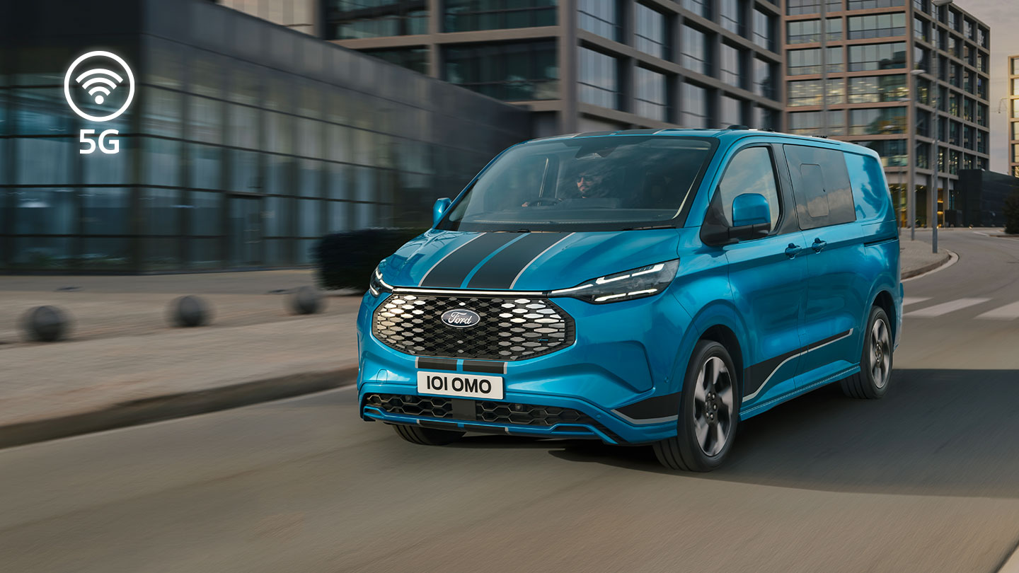 Egy kék Ford E-Transit Custom elektromos áruszállító egy városban halad az úton.